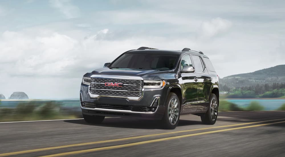 A black 2020 GMC Acadia is shown driving on an open road near a lake.