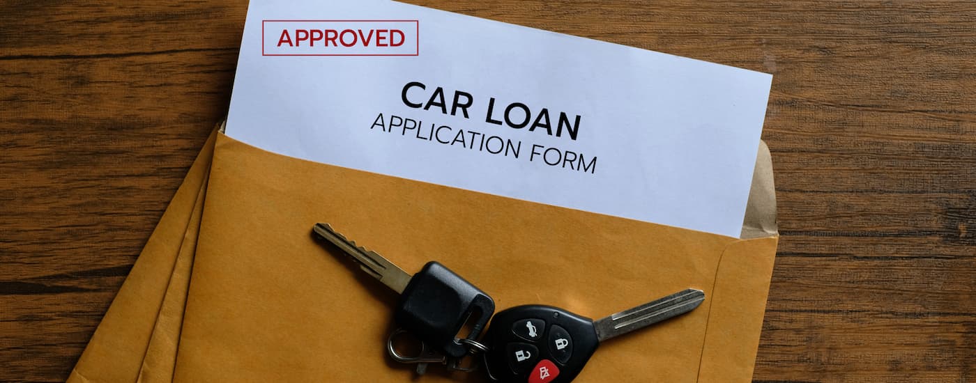A car key is shown on a folder filled with an approved car loan application.