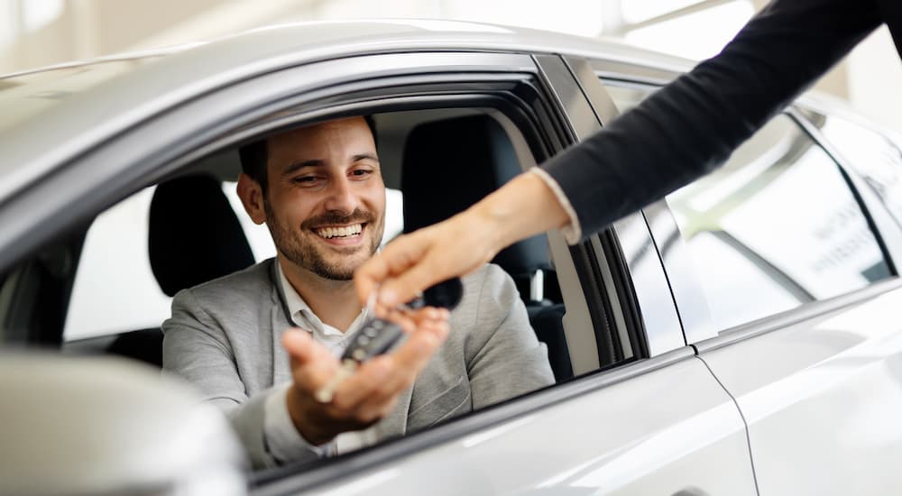 A salesperson is shown passing a car key to a customer. 