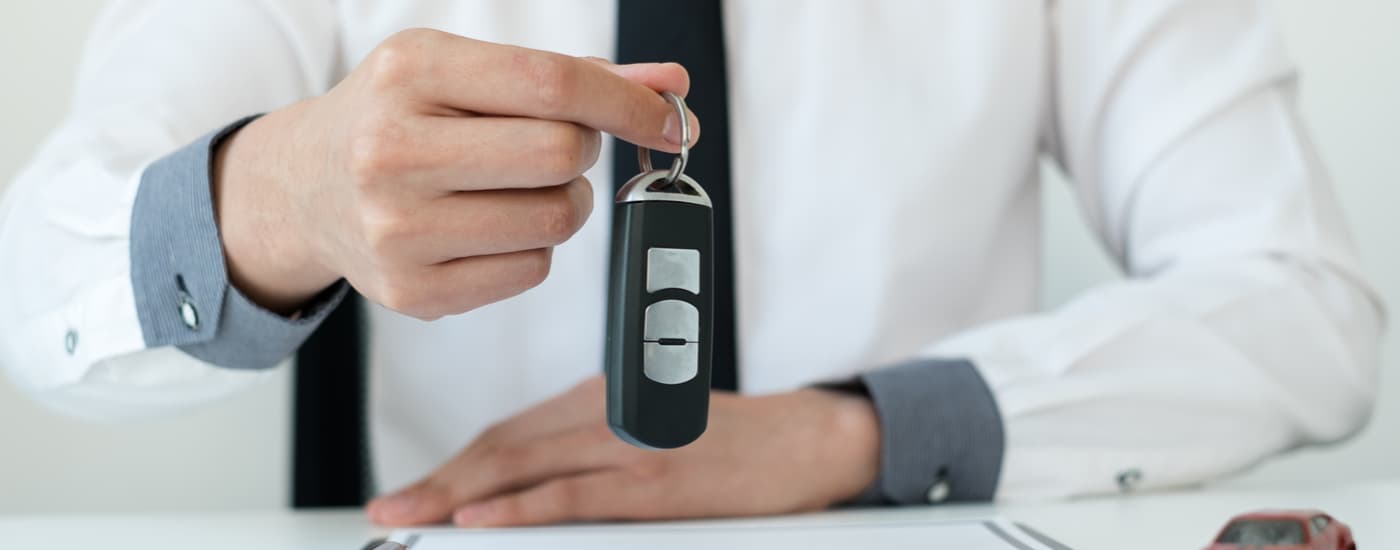 A car salesman is shown holding a car key at a buy here pay here dealership.