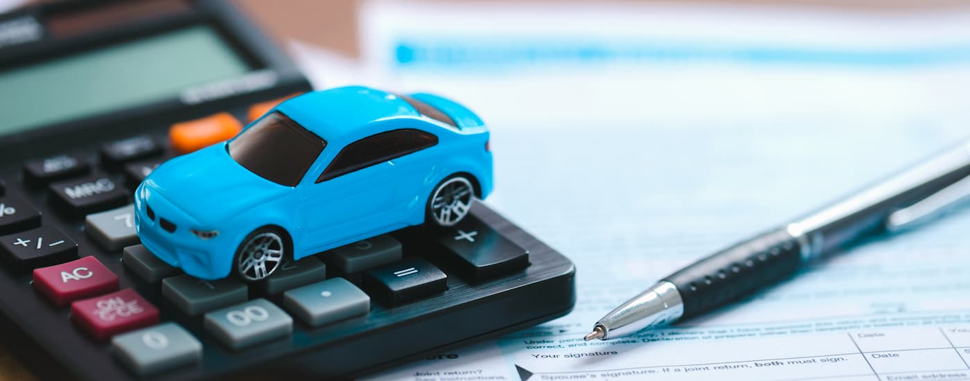 A blue toy car is shown on a calculator is shown on top of financing paperwork.