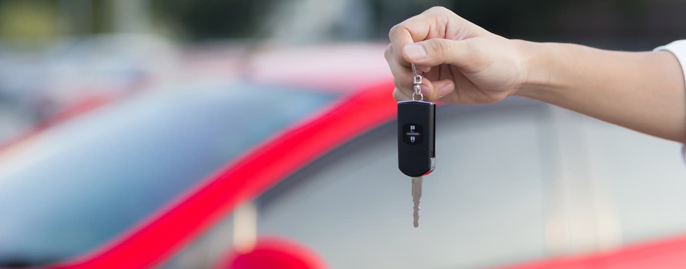A person is shown holding a car key up in front a red vehicle at a car dealership.