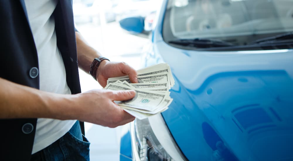 A close up shows a person holding a down payment at a used car dealership.