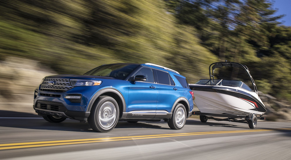 A blue 2020 Ford Explorer Hybrid is shown towing a boat after leaving a used car dealership in Lansing, MI.