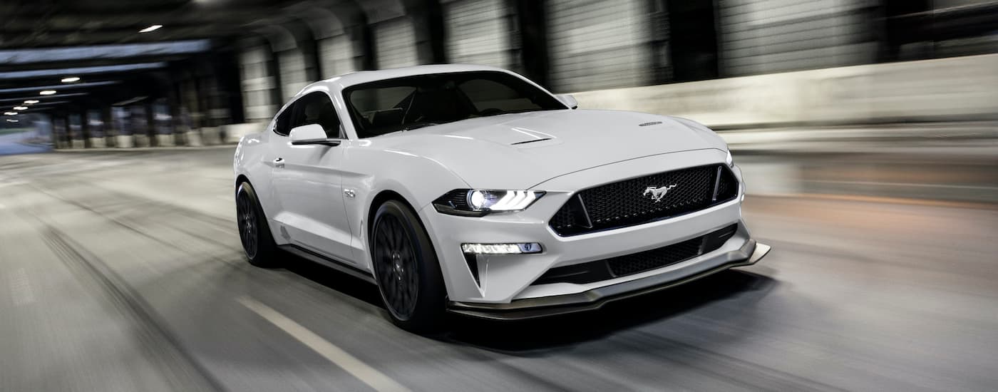 A white 2020 Ford Mustang GT is shown driving through a tunnel after leaving a used car dealership in Lansing MI.