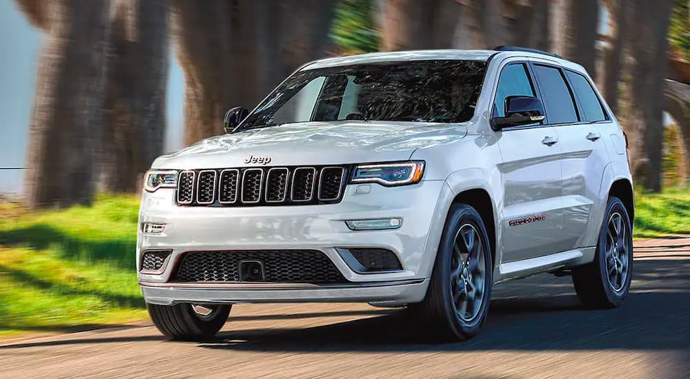 A white 2020 Jeep Grand Cherokee is shown driving on a tree-lined road.