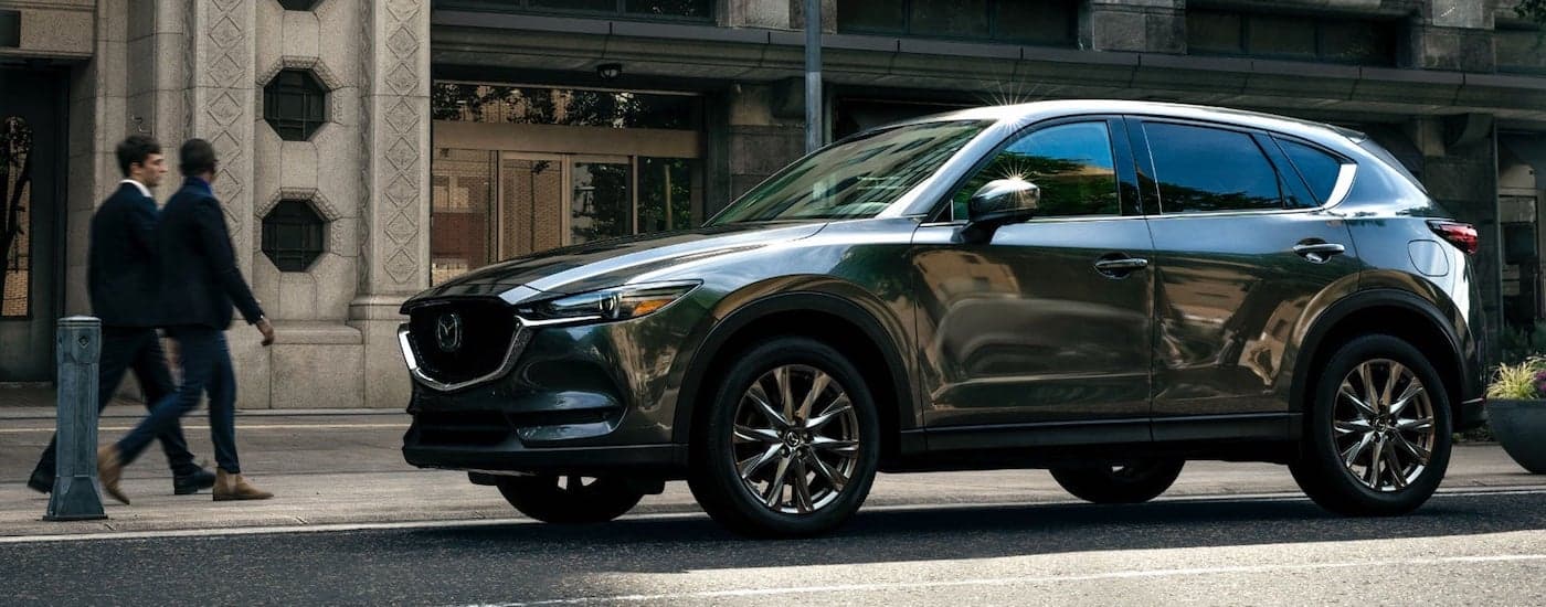 A dark grey 2021 Mazda CX-5 is shown from the side parked on a city street.