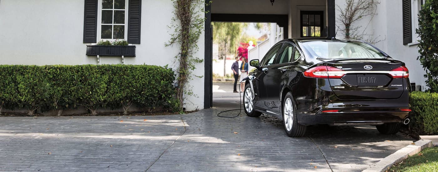 A black 2020 Ford Fusion Hybrid Titanium is shown charging in a driveway.