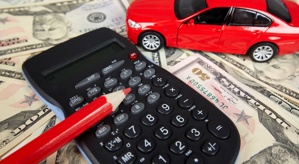 A calculator is shown next to a red toy car on a pile of money.