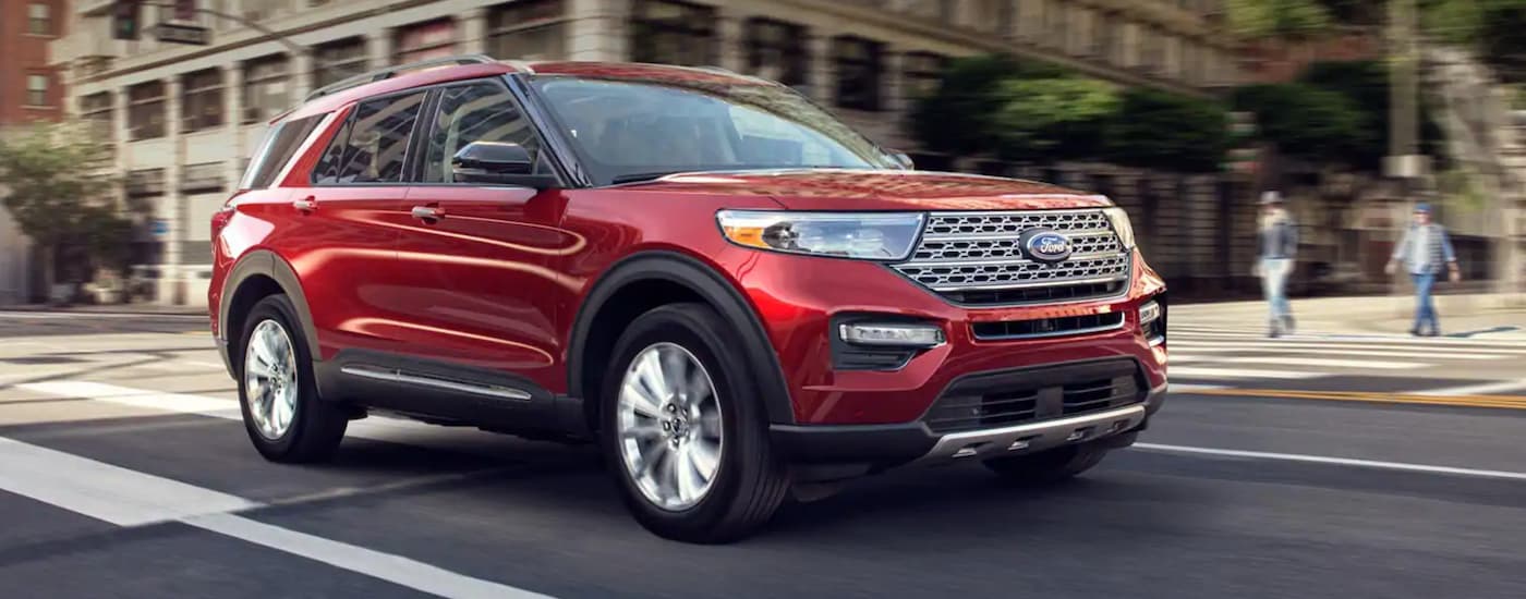 A red 2020 Ford Explorer is shown driving on a city street after viewing used SUVs in Lansing, MI.