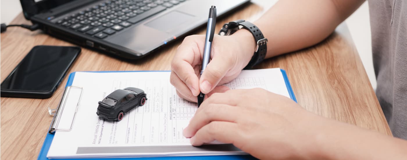A person is shown filling out paperwork for their new vehicle at a used car dealership.