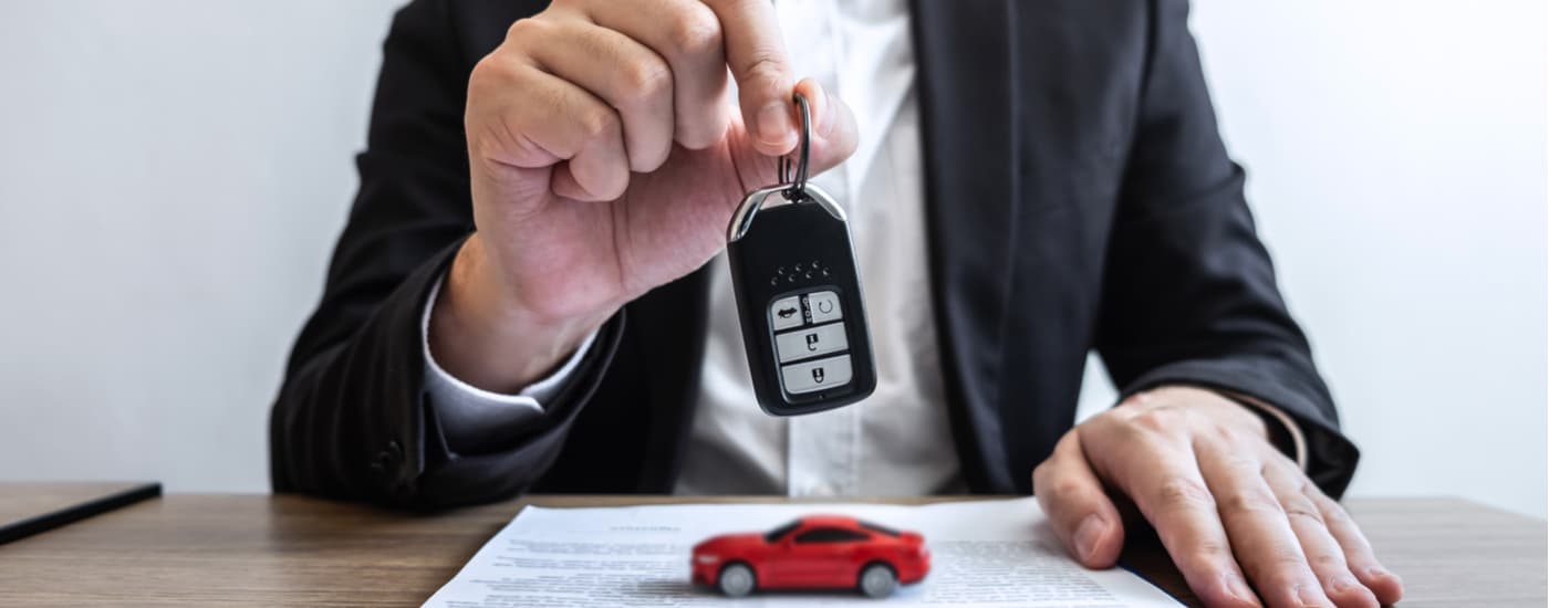 A car salesman is shown holding a car key at a used car dealership.